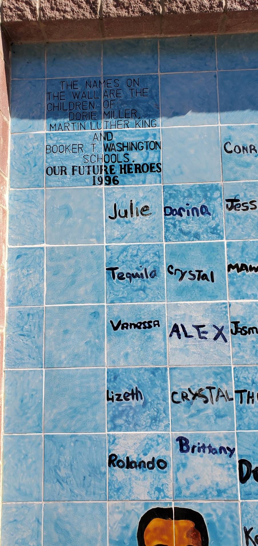 A close up of the passage in the upper left of the Dorie Miller Mural which reads, "The names on the wall are the children of Dorie Miller, Martin Luther King and Booker T Washington schools. Our Future Heroes. 1996"