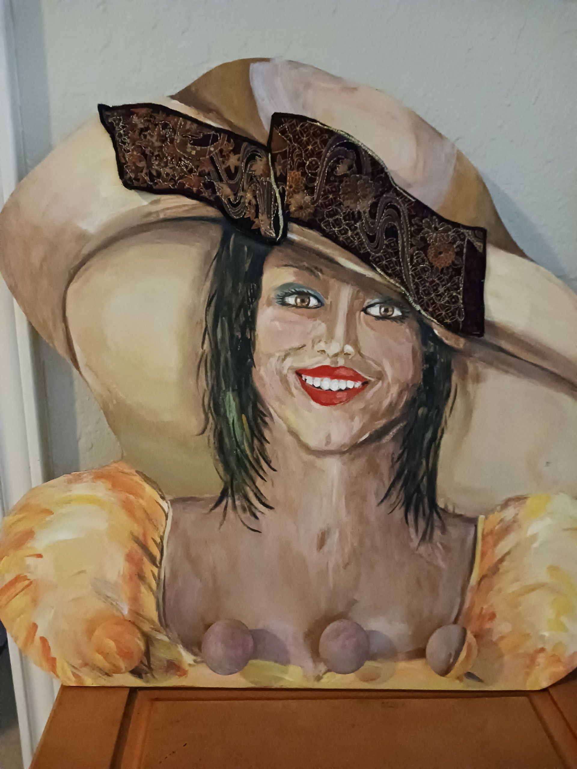 A dark haired woman of color wearing a brown hat and a yellow dress. The hat features a brown cloth accent. Painted onto a wood known as jewelry head.
