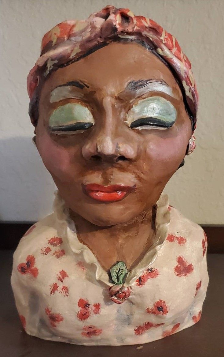 A sculpture of a woman of color wearing a white and red dress, blue eyeshadow, and red lipstick